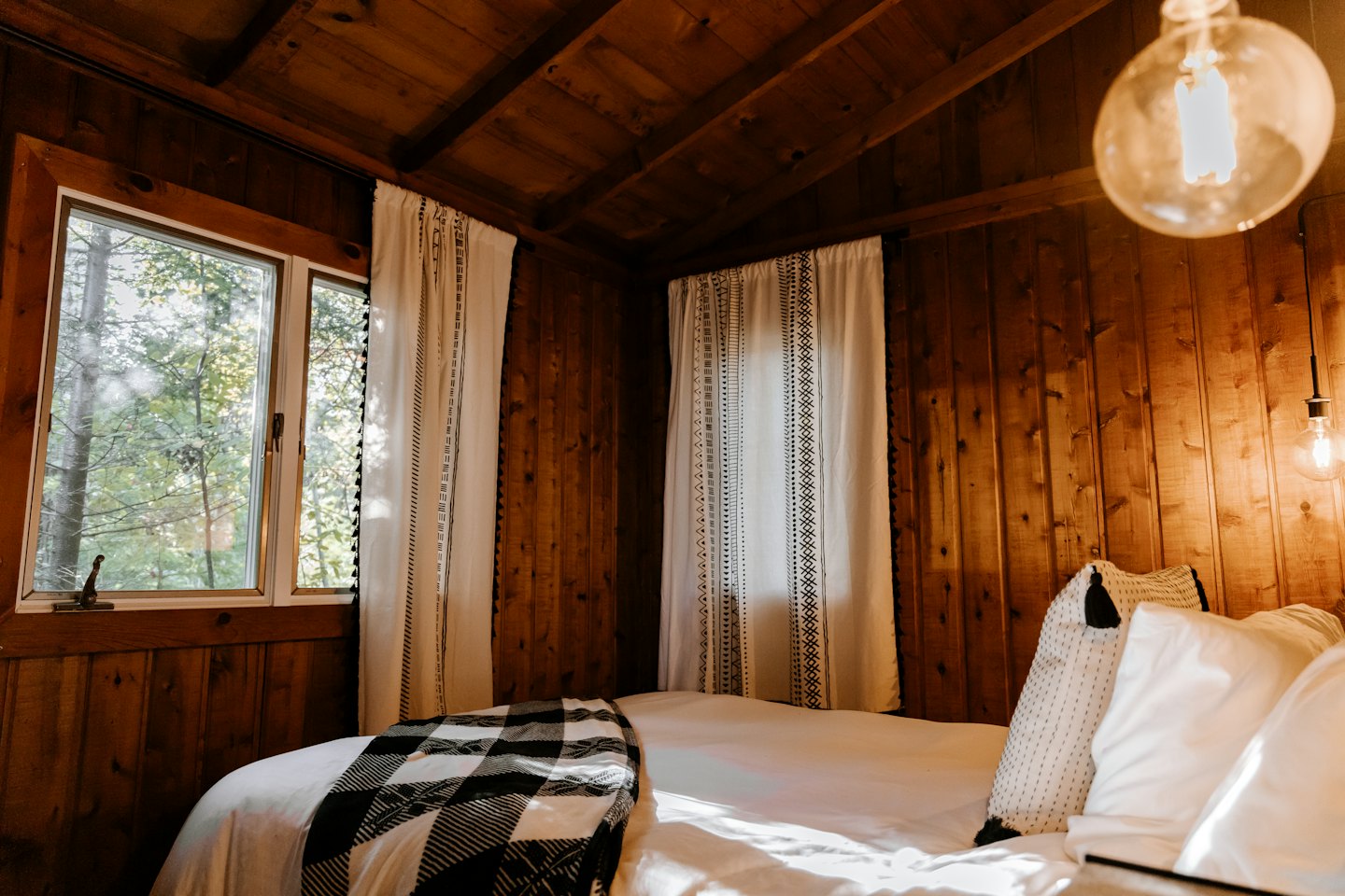 Wooden bedroom with a bed featuring a plaid blanket.