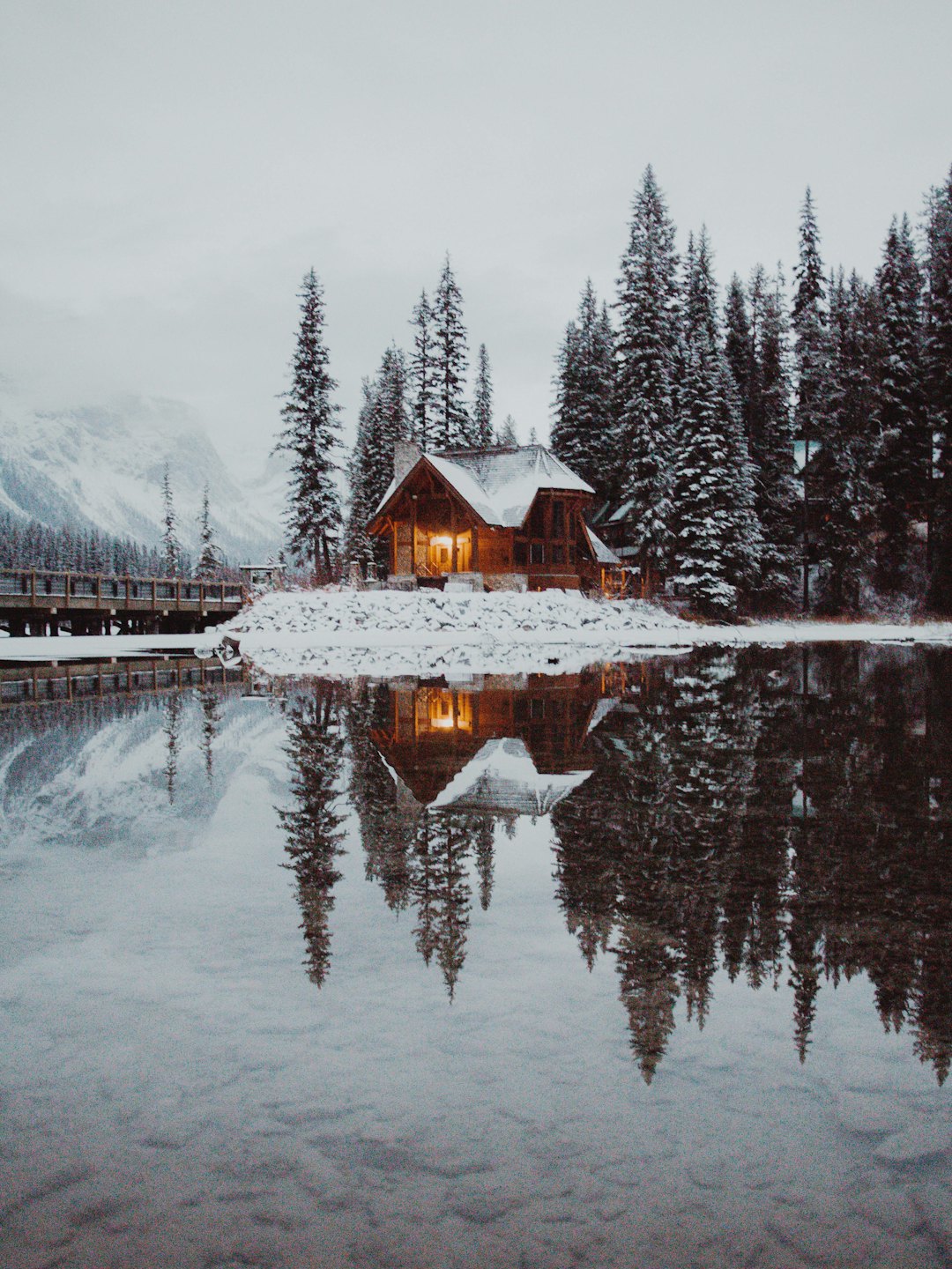 A wooden lodge reflected in a lake surrounded by snowy trees.