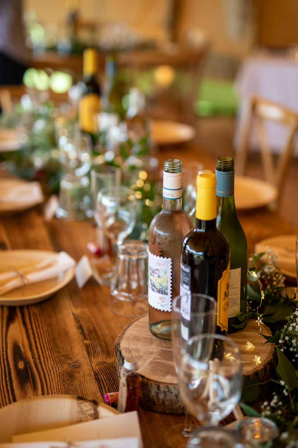 Rustic table set for an event with wine, plates, and foliage.