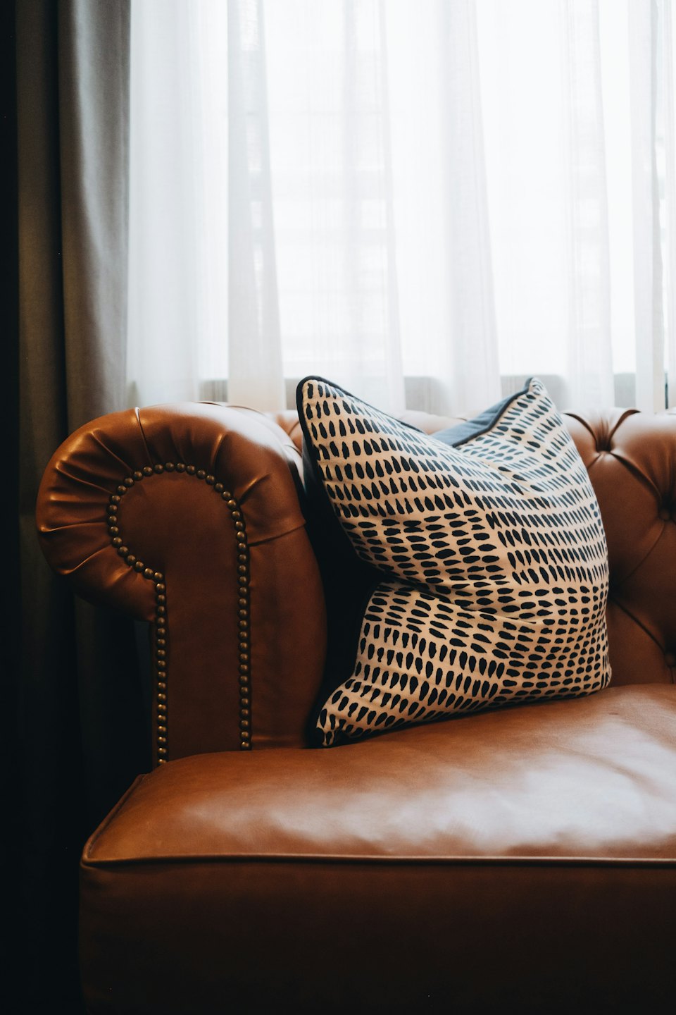 Brown leather tufted armchair with a patterned cushion sits indoors.