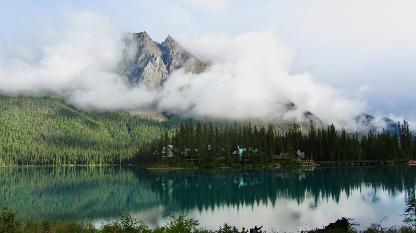 A lodge with turquoise roofs sits on a small island lake.