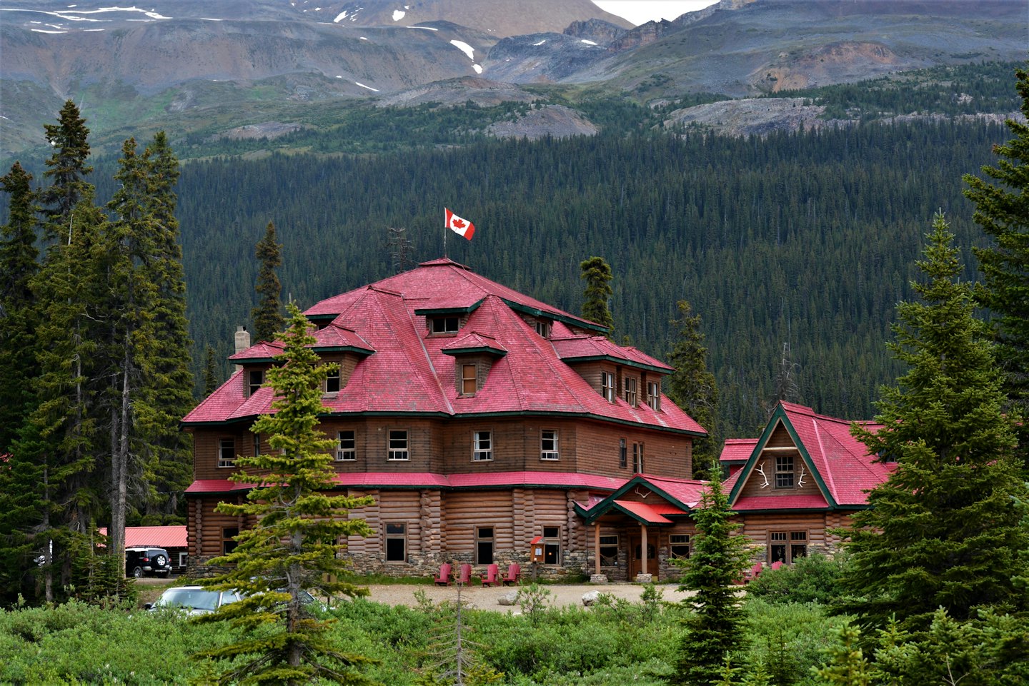 Rustic wooden lodge with a red roof near evergreen trees.